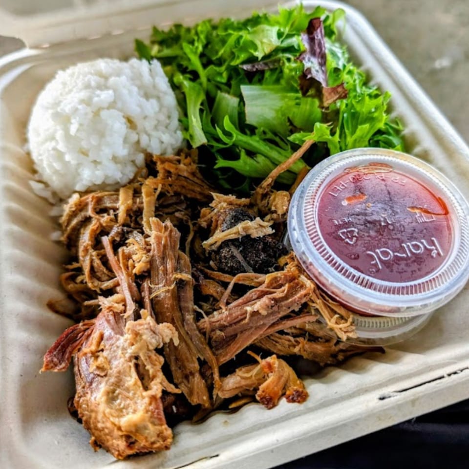 Kono's Hawaiian pulled pork plate with rice, green salad, and a side of sauce in a takeout container.