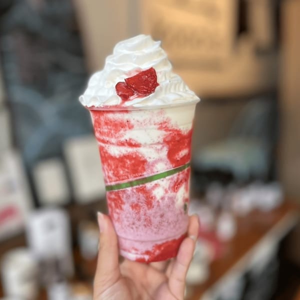 Hand holding a Kono's strawberry smoothie with whipped cream and fresh strawberry pieces.