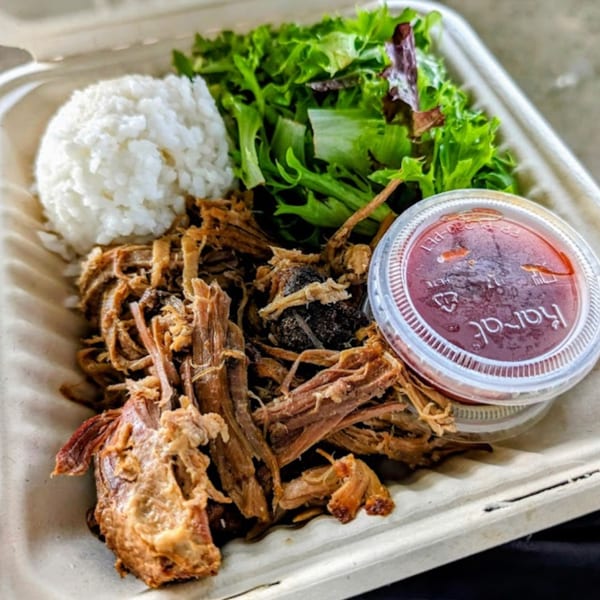 Kono's Hawaiian pulled pork plate with rice, green salad, and a side of sauce in a takeout container.