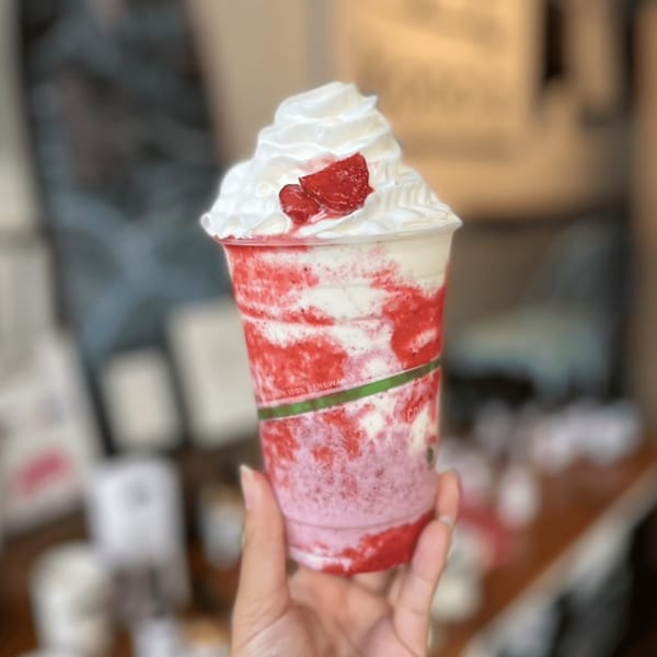 Hand holding a Kono's strawberry smoothie with whipped cream and strawberry pieces.