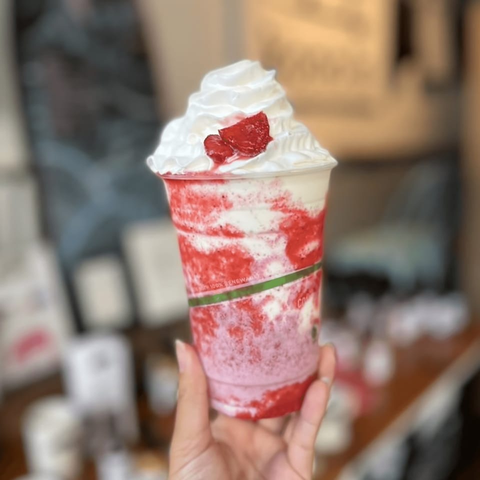 Hand holding a Kono's strawberry smoothie with whipped cream and strawberry pieces.