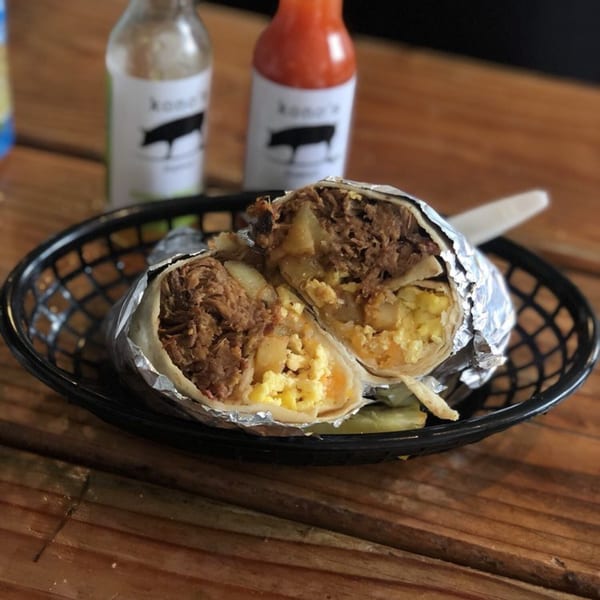 A Kono's breakfast burrito, cut in half, revealing pulled pork, eggs, and potatoes.