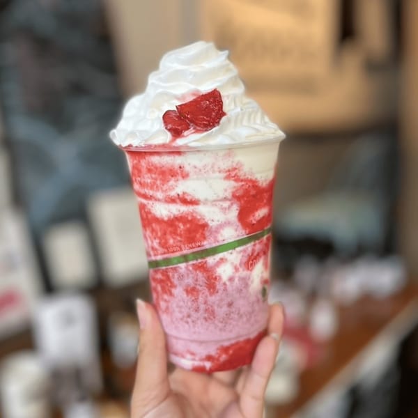 Hand holding a Kono's strawberry smoothie with whipped cream and fresh strawberries.