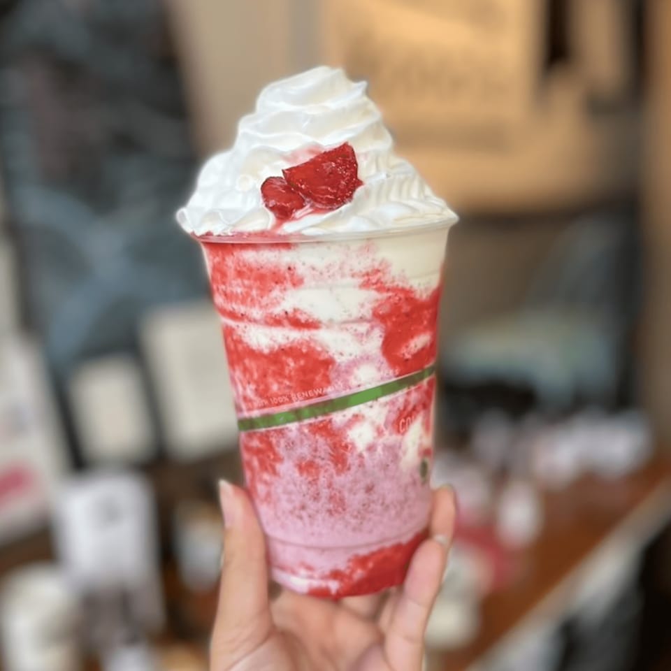 Hand holding a Kono's strawberry smoothie with whipped cream and fresh strawberries.
