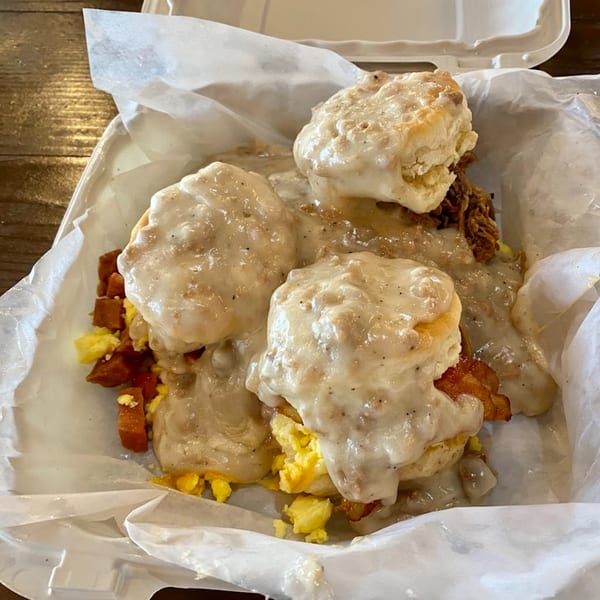 Kono's biscuits and gravy with scrambled eggs, bacon, and pulled pork in a takeout container.