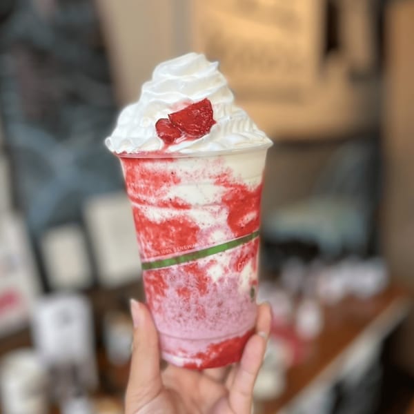 Hand holding a Kono's strawberry smoothie with whipped cream and fresh strawberries.