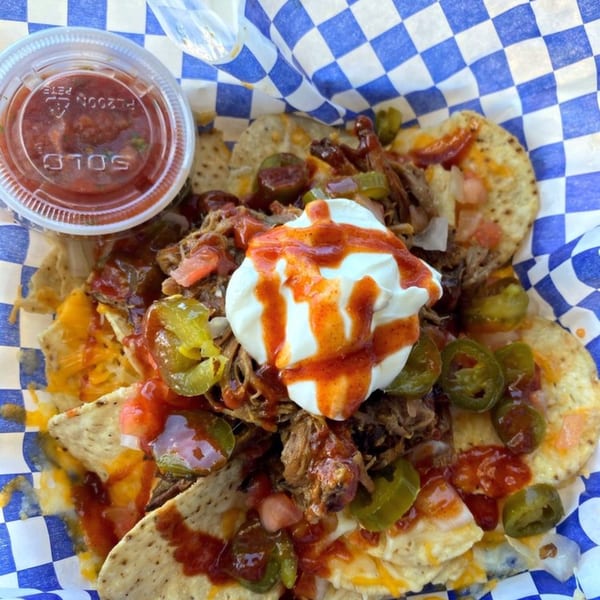 Kono's pulled pork nachos with jalapeños, sour cream, and salsa in a blue checkered basket.
