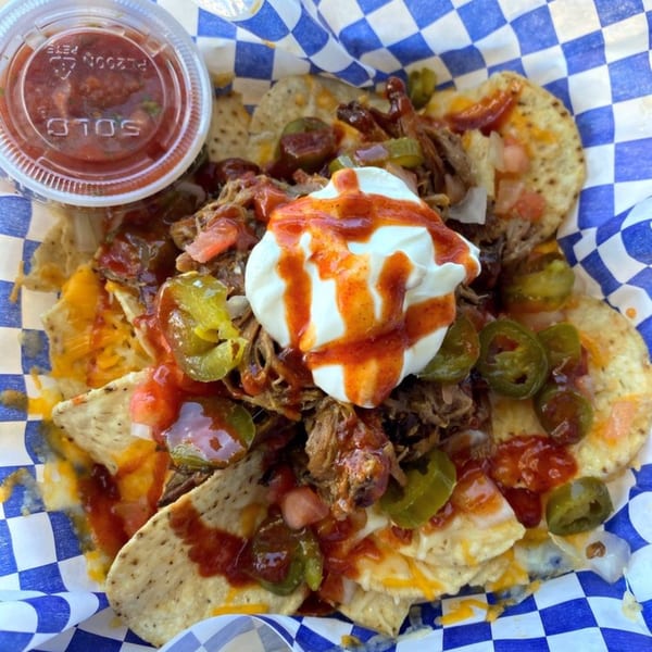 Kono's Hawaiian pulled pork nachos with sour cream, salsa, jalapeños, and cheese on a blue checkered liner.