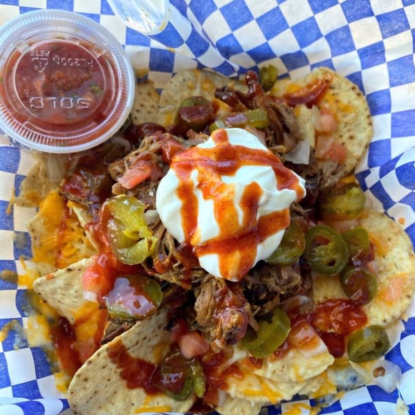 Kono's pulled pork nachos with cheese, jalapeños, salsa, and sour cream in a blue checkered basket.