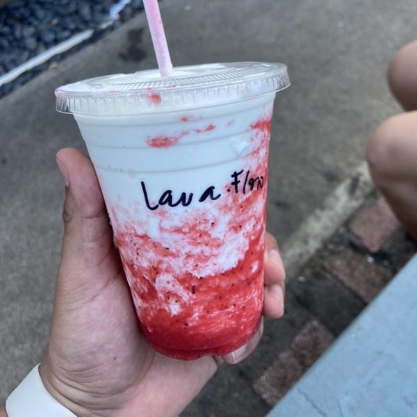 Hand holding a Kono's Lava Flow smoothie with red and white swirls and a pink straw.