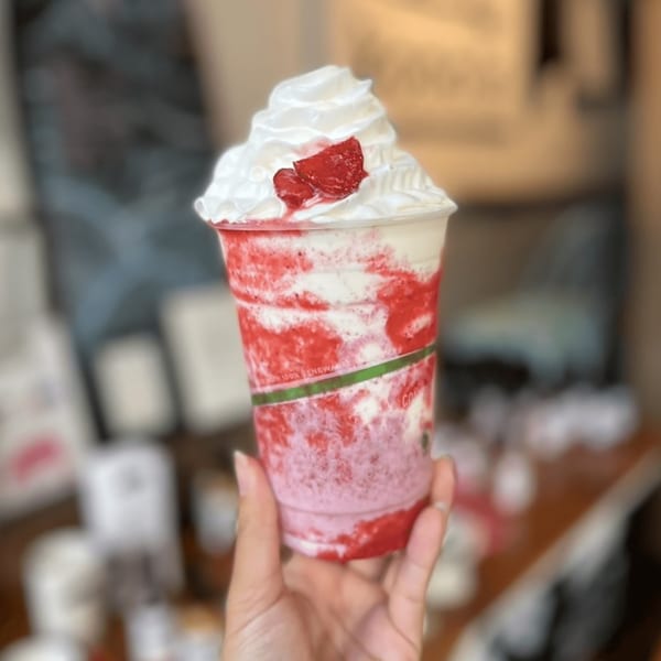 Hand holding a Kono's strawberry smoothie with whipped cream and strawberry pieces on top.