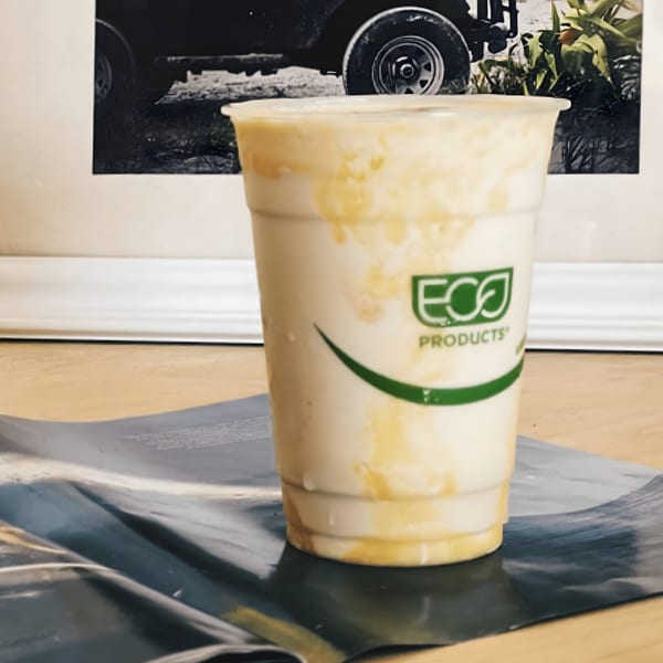 A Kono's Hawaiian smoothie in a clear cup with a green Eco-Products logo, on a table.