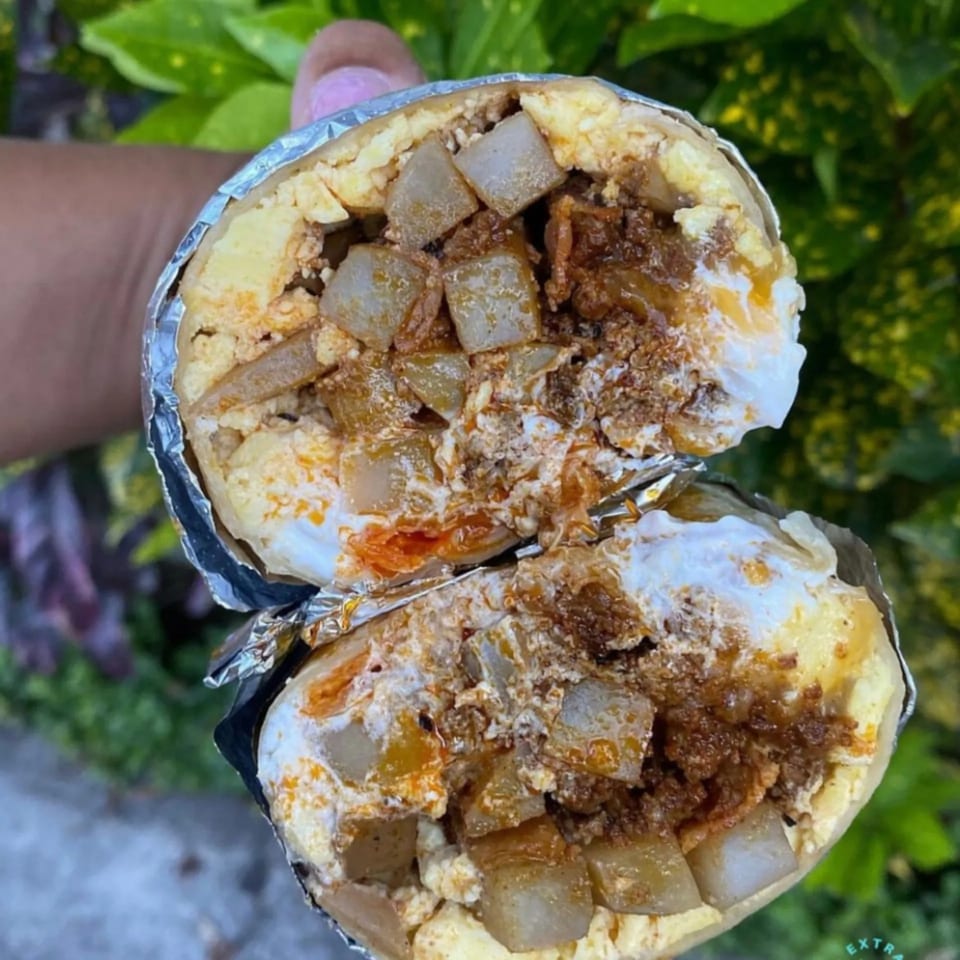 A Kono's breakfast burrito, cut in half, revealing eggs, potatoes, and meat wrapped in foil.