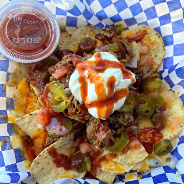 Kono's pulled pork nachos with sour cream, hot sauce, jalapeños, and salsa on a checkered liner.